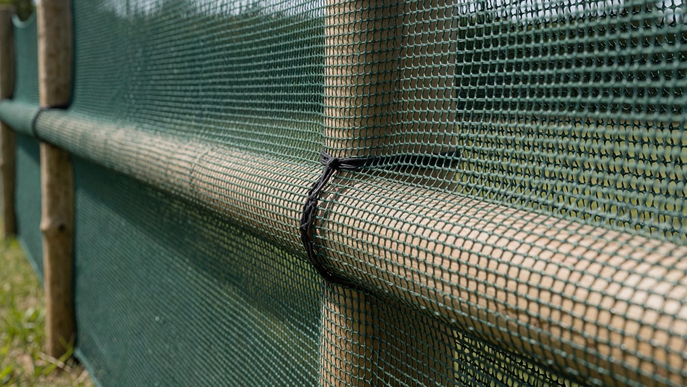 Dark green windbreak mesh netting tensioned tightly on a wooden post-and-rail frame
